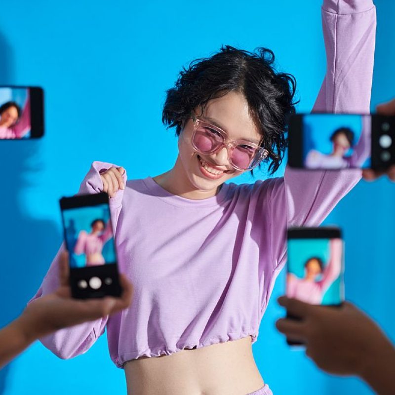 Happy teenage blogger posing when subscribers photographing her on smartphones
